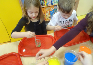 Troje dzieci nalewa pipetami zabarwioną dzieci do słoiczka z olejem.